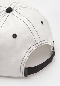 Fehér sapka ellentétes fekete varrással és állítható pánttal. Lekerekített koronájú, oldalán egy kis logó címkével.