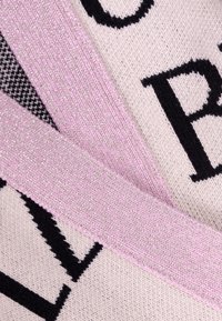 Zbliżenie na dzianinę z czarnymi literami na jasnym tle, na które nałożony jest błyszczący, różowo-czarny paskowy materiał.