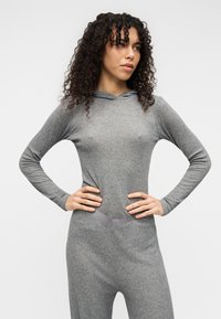 Γκρι ολόσωμη φορμα με κουκούλα, μακριά μανίκια, ριμπ υφή και εφαρμοστή γραμμή. Διαθέτει αντίθετη λείου υφής ζώνη στη μέση.