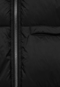 Black puffer jacket with a shiny silver zipper, featuring a horizontal quilted texture and a small pocket on the front.