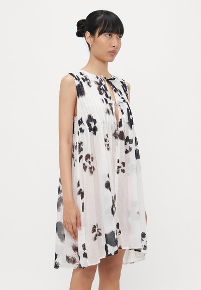 Abito senza maniche realizzato in tessuto leggero con una base bianca e motivi floreali in bianco e nero simili a acquerelli. Presenta un design plissettato e un dettaglio a chiave.
