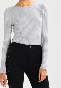 Grå räfflad långärmad topp i kombination med högmidjade svarta byxor med sidoknappning och silverfärgad knappstängning.