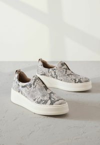 Baskets à enfiler avec un motif texturé en imprimé serpent noir et blanc. Elles sont dotées d'une semelle plateforme blanche et d'accents élastiques sur les côtés.