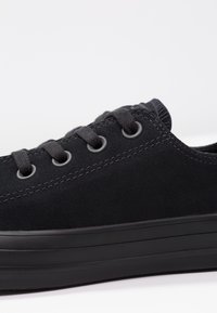 ČernéSemišové boty s kulatou špičkou a plochou černou gumovou podrážkou. Obsahují černé oka a šněrování, s kontrastním prošíváním na svršku.