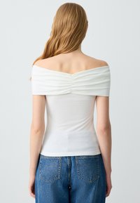 Weißes, schulterfreies Ripptop mit geraffter Rückennaht, kombiniert mit hochgeschnittenen blauen Jeans.