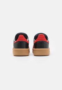 Svarte lær sneakers med røde semskede detaljer, hvite elementer og en teksturert gummisåle. Rund form med polstrede krager for komfort.