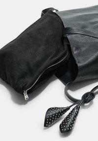 Czarna skórzana torba z zamszowymi akcentami, zamknięciem na zamek błyskawiczny i szpiczastymi ozdobami. Posiada teksturowaną powierzchnię oraz regulowane paski.