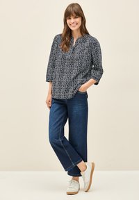 Blusa azul marino con estampado, escote en V y mangas tres cuartos, combinada con pantalones vaqueros de pierna ancha en denim oscuro y zapatillas blancas.
