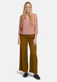 Chemisier à manches longues avec un motif géométrique rouge et blanc, associé à un pantalon large vert olive et des chaussures à plateforme noires.