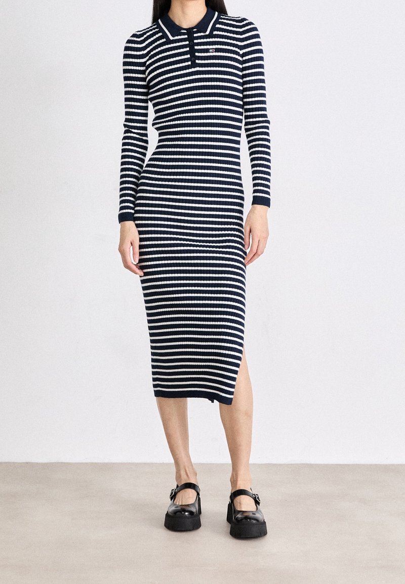 Femme portant une robe midi à manches longues rayée horizontale bleu marine et blanc avec col et des chaussures Mary Jane noires.