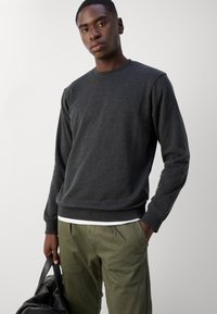 Pull gris foncé avec un col rond et des manches longues. Le tissu semble doux, associé à un pantalon vert clair et un sac noir.