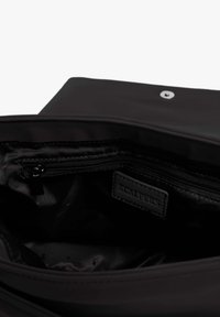 Interior de una bolsa negra de tela con un bolsillo con cremallera y una etiqueta de cuero etiquetada "SCALPERS". Textura suave, diseño minimalista y sin patrones.