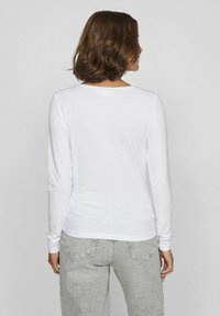 Långärmad vit skjorta i mjukt tyg, med rund halsringning och en figursydd design, kombinerad med ljusgrå jeans.