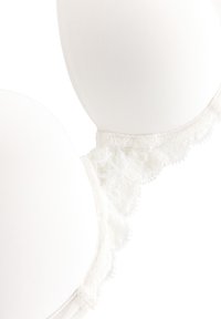 Bílá podprsenka s krajkovým lemem, vybavená hladkými tvarovanými košíčky, detailními krajkovými okraji a nastavitelnými ramínky. Látka působí měkce a jemně.