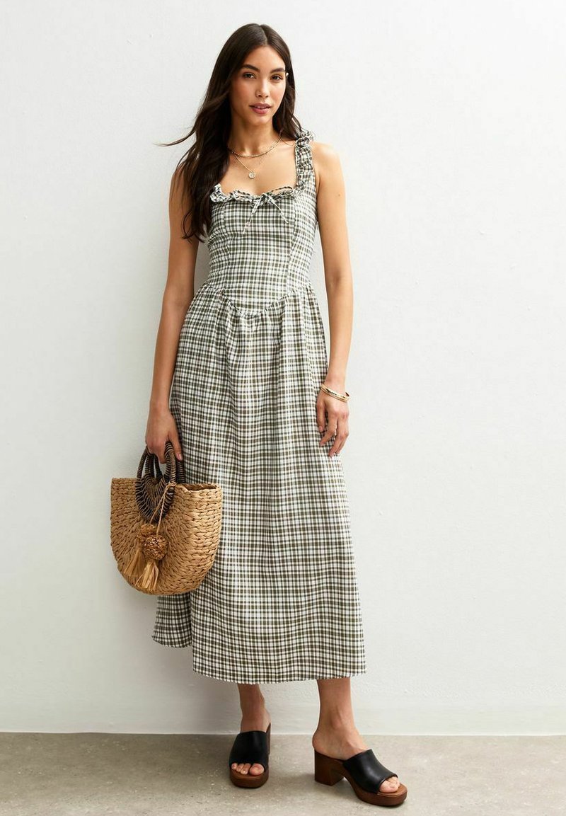 Groen en wit geruite midi-jurk met volantsbandjes, getailleerde lijfje en geplooide taille, gecombineerd met een geweven tas en zwarte slidesandalen.