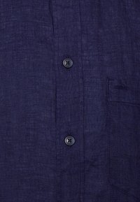 Navy linen shirt with a textured finish, featuring black buttons, a chest pocket, and a button-down collar.