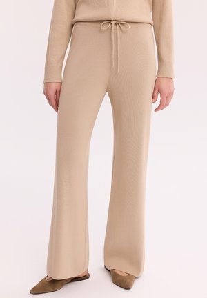 Beżowe szerokie spodnie dzianinowe z wiązanym paskiem w talii, noszone z dopasowanym topem i brązowymi wsuwanymi butami z szpiczastym noskiem.