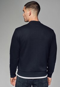 Sweatshirt bleu marine à manches longues et col côtelé, avec une texture lisse et une taille ajustée. Vue de dos avec des coutures minimales.