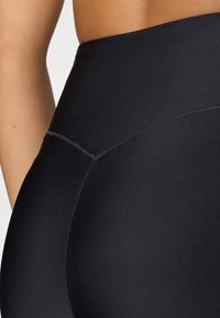 Juodos aukštu liemeniu leggingai su lygiu, tempimu pasiūtu audiniu. Ypatumai: siūlių detalės iš šonų ir be siūlių liemuo patogumui.
