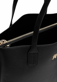 Zwarte leren tote-bag met een textuurafwerking, voorzien van een gouden rits en embleem. Open bovenkant met twee hengsels voor gemakkelijk dragen.