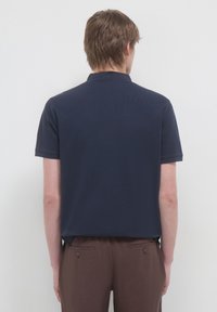 Polo navy in cotone morbido con colletto classico, maniche corte e orlo dritto, abbinato a pantaloni marroni.