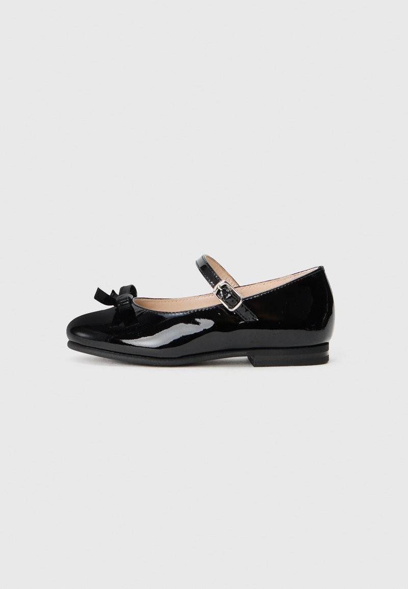 Bottines Mary Jane en cuir verni noir avec une pointe arrondie, un petit nœud décoratif sur le bout et une bride ajustable à la cheville.