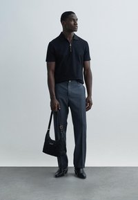 Juoda trumpomis rankovėmis polo marškinėliai su užtrauktuku apykaklėje, pilkos pritaikytos kelnės, juoda dygsniuota peties rankinė ir juodi batai. Paprastas ir modernus dizainas.