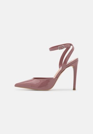Zapato de tacón puntiagudo de charol rosa con una delgada correa en el tobillo y tacón de aguja. Textura suave y acabado brillante.