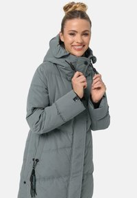 Chaqueta acolchada gris con un alto cuello, capucha con cordón y cierre frontal con cremallera. Presenta un diseño acolchado, bolsillos laterales y acentos negros contrastantes.