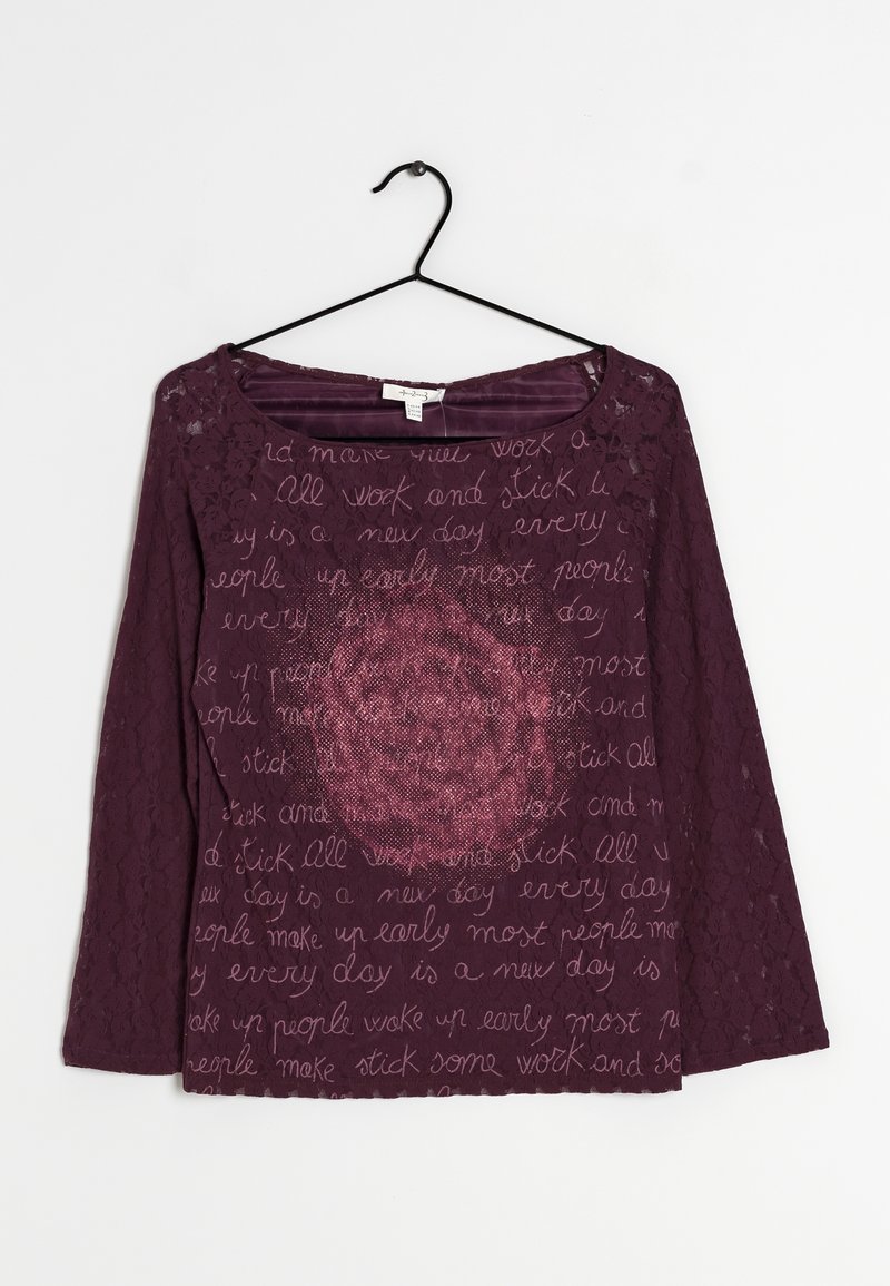 Lila spetstopp med trekvartsärmar, med ett textmönster och en central blommig design i mörkare lila nyanser.