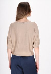 Beige afslappet top med korte, puflede ærmer. Textureret stof. Rund halsudskæring og løs pasform. Bagsiden har en subtil sømdetalje.