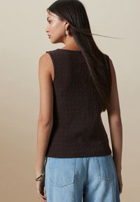 Top fără mâneci, maro închis, texturat, cu decolteu rotund, asortat cu blugi azul deschis cu talie înaltă. Design simplu și curat.