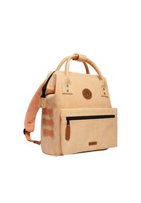 Sac à dos en velours côtelé beige avec poignées doubles, bandoulière rembourrée, poche zippée à l'avant et patch logo. Il présente un tissu texturé et des accents contrastants.