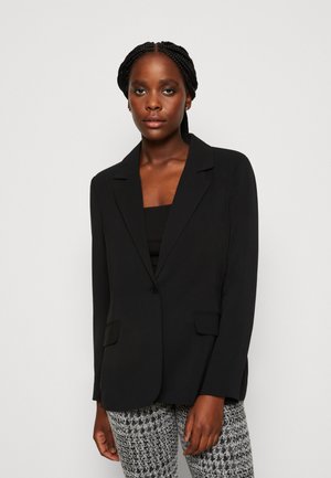 Blazer nero con revers a punta, chiusura a un bottone, due tasche frontali e maniche lunghe, abbinato a pantaloni a fantasia. Texture liscia.
