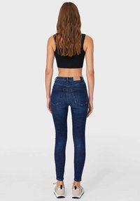 Vaqueros ajustados en denim azul oscuro con una textura suave. Diseño de cintura alta, con bolsillos traseros y un parche con el logotipo en la cinturilla.