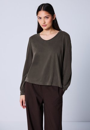 Olijfgroen langellaag top in een relaxte pasvorm met een ronde halslijn. Zachte stof en gathered manchetten. Gepaard met donkere streep-pantalons.