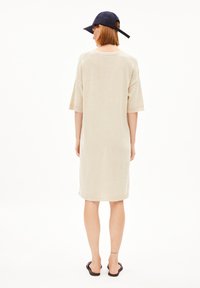 Beige knit dress with short sleeves, knee-length, and ribbed hems. Worn with a navy cap and black sandals, showing a relaxed fit.