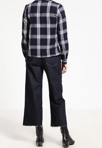 Mörkblå och vit rutigt knäppskjorta med lång ärm, matchad med vida mörk denimjeans och svarta ankelboots.