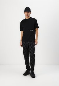 Črna bombažna majica s belim logotipom na prsih, v kombinaciji s črnimi hlačami s svetlečimi vzorci, ki imajo houndstooth vzorec in elastične manšete. Črne športne čevlje.