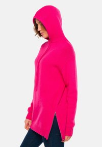Sweat à capuche rose avec fermeture éclair et fentes sur les côtés. Fabriqué à partir de matériau doux, il possède des manches longues et une coupe décontractée.
