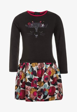 Černé šaty s dlouhým rukávem a výšivkou kočičí tváře, s barevným květinovým sukní s různorodým vzorem a nabíranou texturou.