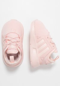 Ljust rosa mesh-sneakers med gummisulor, med tre horisontella ränder, texturerade ytor och en dragflik vid hälen för enkel påtagning.