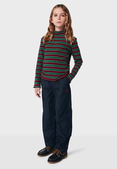 Randig långärmad topp i grönt och rött ribbat material, i kombination med mörkblå randiga byxor. Svarta skor med bruna detaljer.
