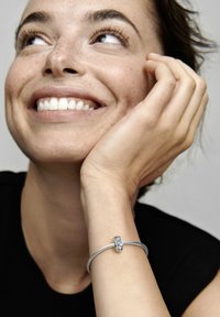 Srebrna zapestnica z zapletenim oblikovanjem, opremljena s pravokotnim zaponko, okrašena z modrimi in prozornimi dragulji.