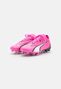 Scarpette da calcio rosa con tomaia in rete, accenti neri e bianchi, superficie testurizzata e tacchetti trasparenti per aderenza.