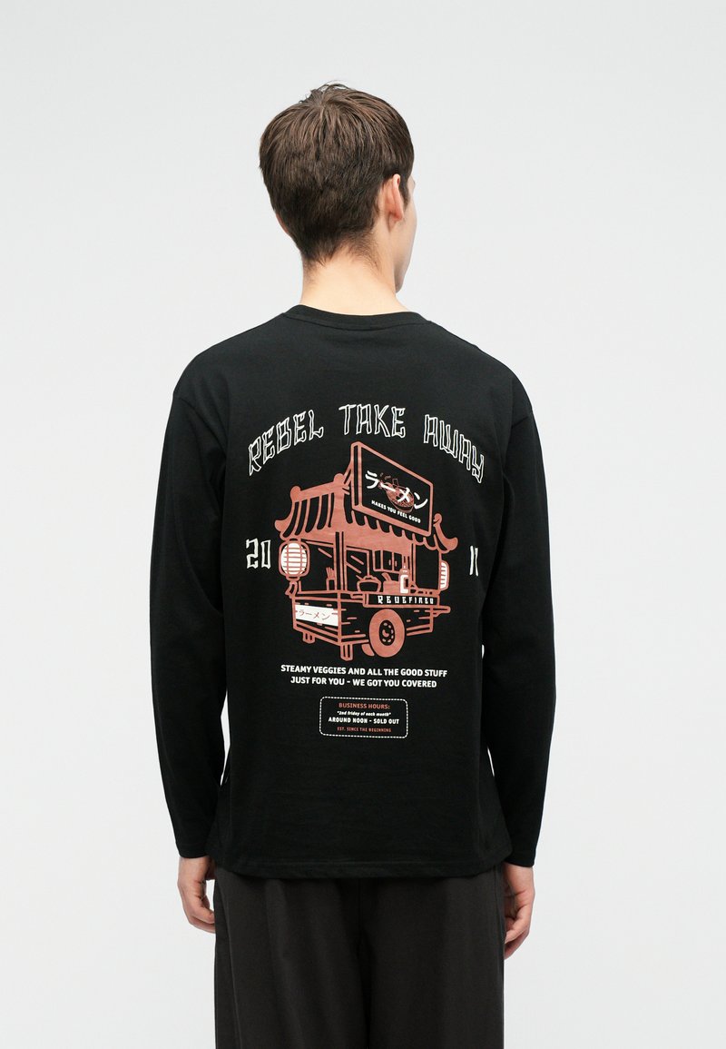 Bărbat îmbrăcat cu o cămașă neagră cu mâneci lungi, având un grafic cu un cărucior de mâncare roz și textul "Rebel Take Away" plus alte inscripții mai mici pe spate.