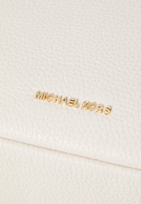 White textured leather purse featuring a gold "MICHAEL KORS" logo. The surface shows a pebbled finish with a distinctive, crisp edge.