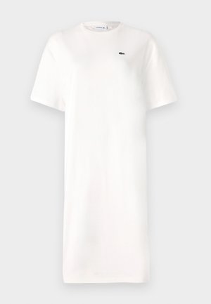 Robe t-shirt blanche en coton, à col rond, à manches courtes, avec un petit logo vert sur la poitrine. Silhouette simple et droite.