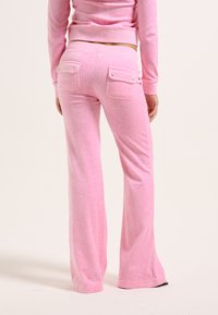 Rosa Jogger-Hosen aus weichem Material, mit Rückentaschen und dekorativen Knöpfen. Glatte Textur und ausgestellter Schnitt.