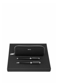 Ensemble stylo noir et crayon avec accents argentés, disposés sur une boîte rectangulaire noire accompagnée d'une housse noire zippée assortie portant l'inscription « BOSS ».